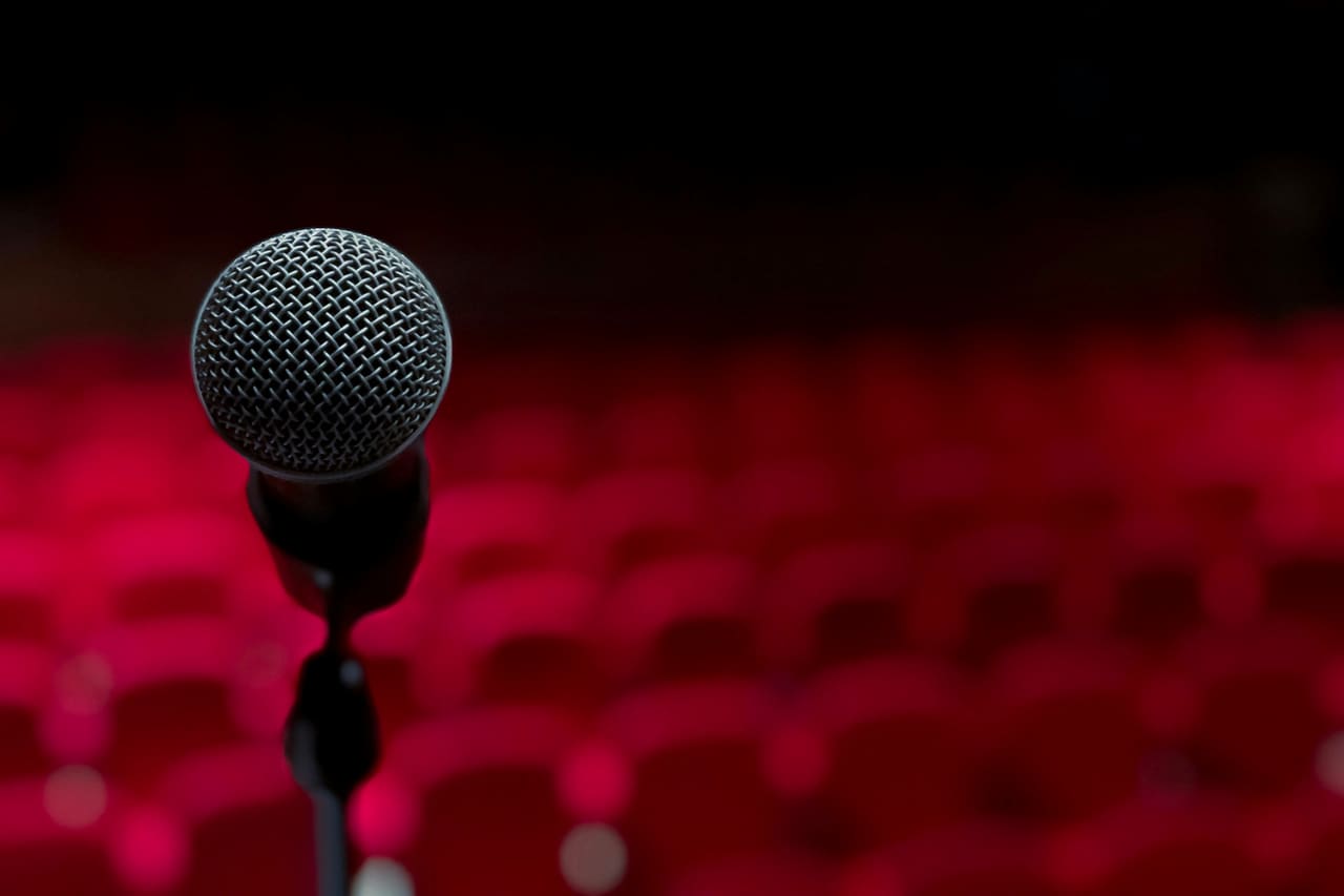 A microphone on a stand in front of rows of red theatre seats