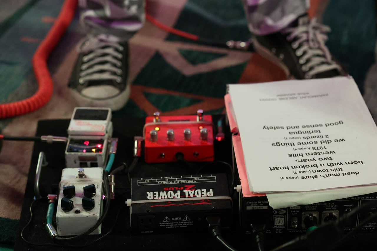 A printed set list lying on a guitar pedalboard beside a pair of sneakers